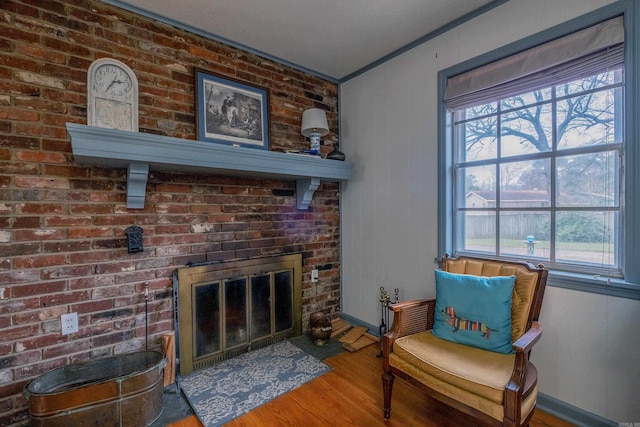 living area with plenty of natural light, wood-type flooring, crown molding, and a brick fireplace