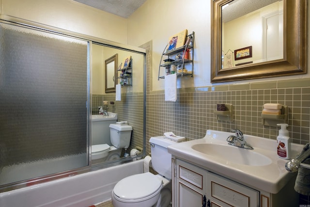 full bathroom with bath / shower combo with glass door, a textured ceiling, toilet, vanity, and tile walls