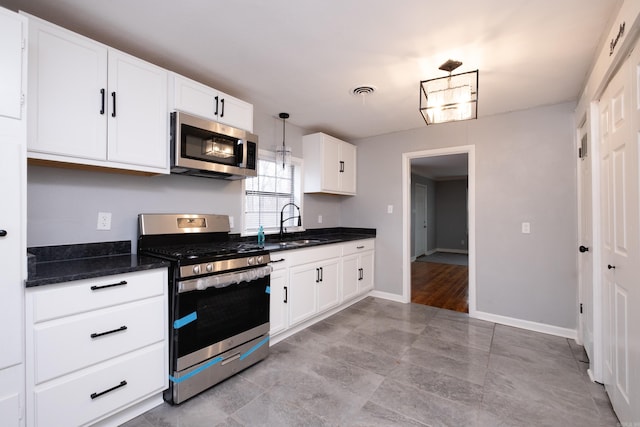 kitchen with pendant lighting, white cabinets, sink, dark stone countertops, and stainless steel appliances