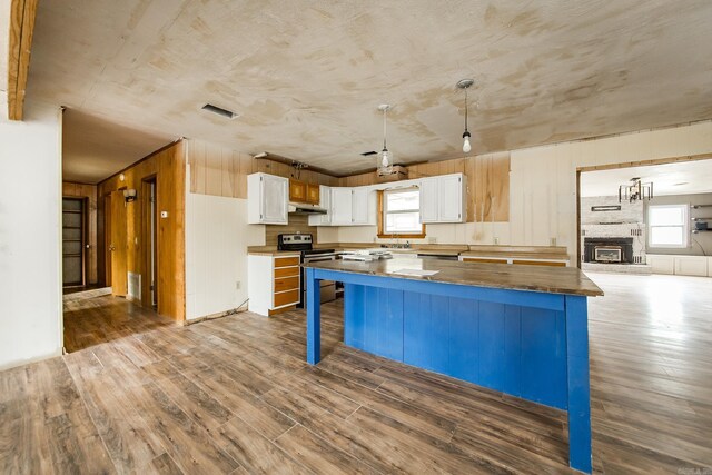 kitchen featuring stainless steel range with electric stovetop, white cabinets, hardwood / wood-style flooring, a fireplace, and a kitchen bar