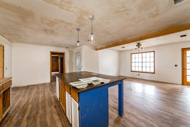 kitchen with ceiling fan, hanging light fixtures, a kitchen breakfast bar, dark hardwood / wood-style flooring, and beamed ceiling