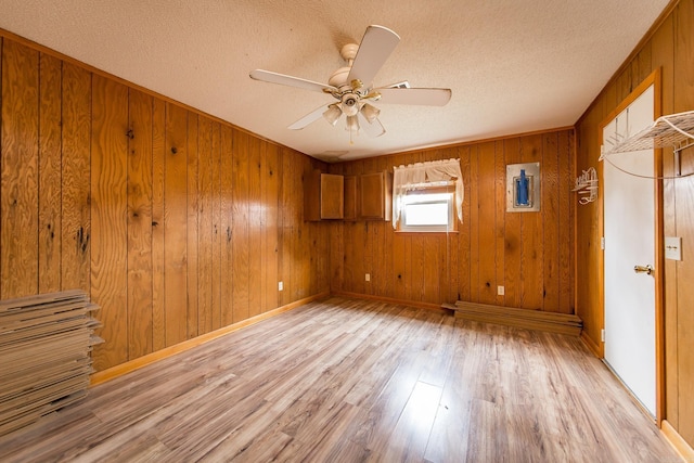 spare room featuring a textured ceiling, light wood-type flooring, ceiling fan, and wooden walls