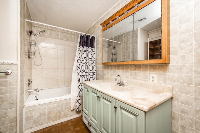 bathroom with a textured ceiling, vanity, shower / bathtub combination with curtain, and tile walls