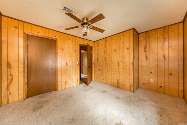 unfurnished bedroom featuring wood walls, ceiling fan, ornamental molding, a textured ceiling, and carpet floors