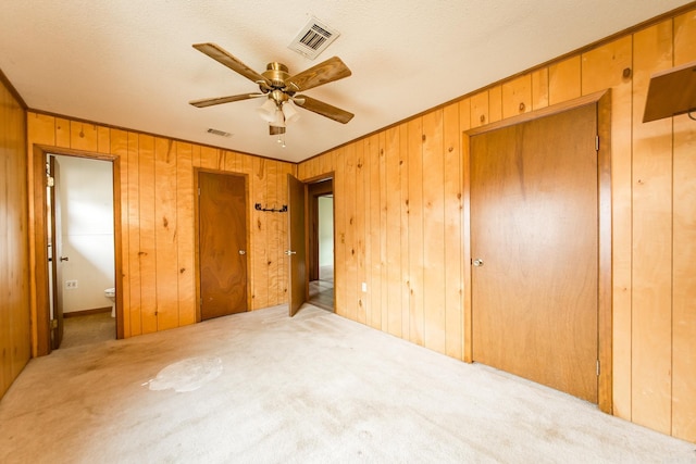 unfurnished bedroom featuring light colored carpet, ceiling fan, and wooden walls