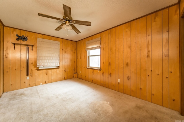 carpeted empty room featuring a textured ceiling, ceiling fan, and wooden walls