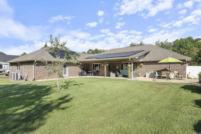 back of property with a yard, a patio, central AC unit, and solar panels