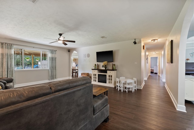 living room with ceiling fan, a fireplace, and dark wood-type flooring