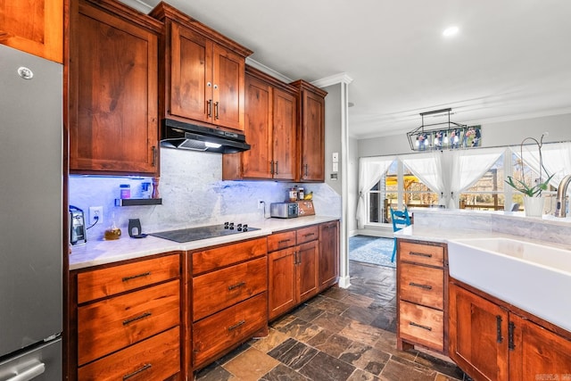 kitchen featuring decorative backsplash, black electric cooktop, crown molding, sink, and stainless steel refrigerator