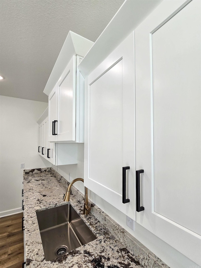 kitchen with white cabinetry, sink, light stone countertops, dark wood-type flooring, and a textured ceiling