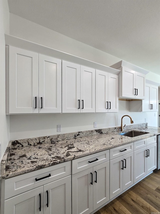 kitchen with light stone counters, sink, white cabinets, and dark wood-type flooring