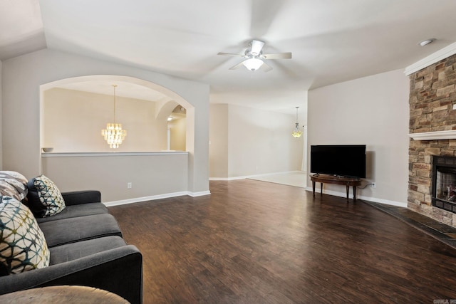 living room with ceiling fan with notable chandelier, a stone fireplace, dark wood-type flooring, and vaulted ceiling