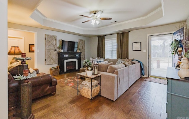 living room featuring hardwood / wood-style flooring, ceiling fan, a fireplace, and a tray ceiling