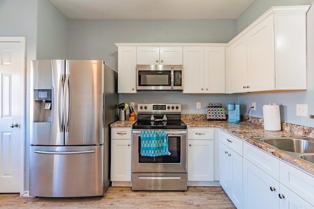 kitchen with light stone countertops, white cabinetry, stainless steel appliances, and light wood-type flooring