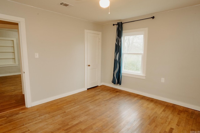 empty room with ceiling fan, built in features, and light wood-type flooring