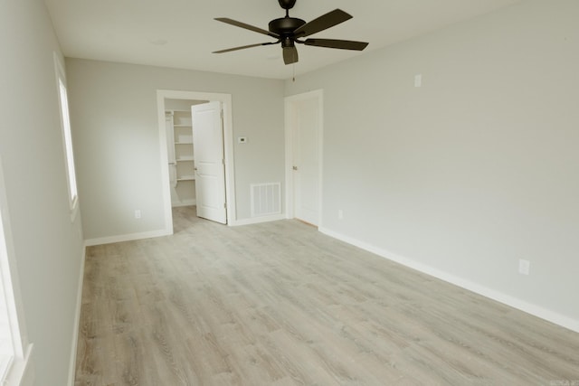 unfurnished bedroom featuring ceiling fan, a walk in closet, light hardwood / wood-style flooring, and a closet