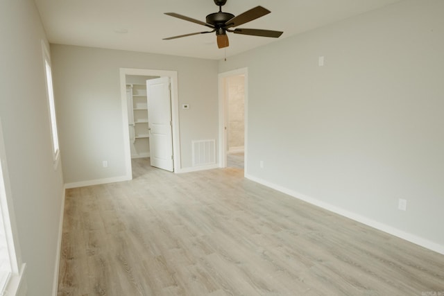 unfurnished bedroom featuring light wood-type flooring, a walk in closet, a closet, and ceiling fan