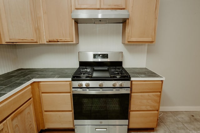 kitchen with tile countertops, light brown cabinetry, light tile patterned floors, and stainless steel range with gas stovetop