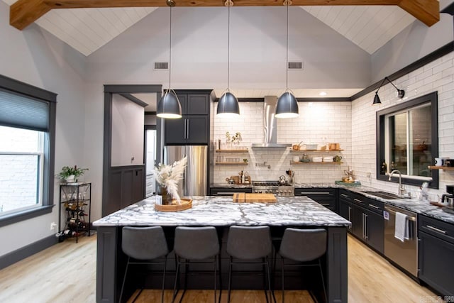 kitchen with light stone counters, stainless steel appliances, sink, decorative light fixtures, and a kitchen island