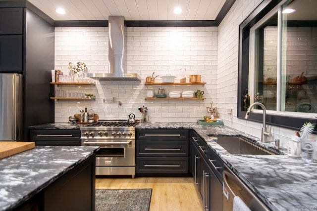 kitchen featuring wall chimney exhaust hood, sink, appliances with stainless steel finishes, and dark stone counters