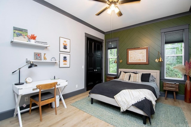 bedroom with ceiling fan, wooden walls, wood-type flooring, and ornamental molding