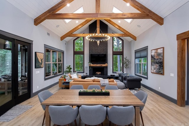 dining room featuring light wood-type flooring, a skylight, beam ceiling, high vaulted ceiling, and a chandelier