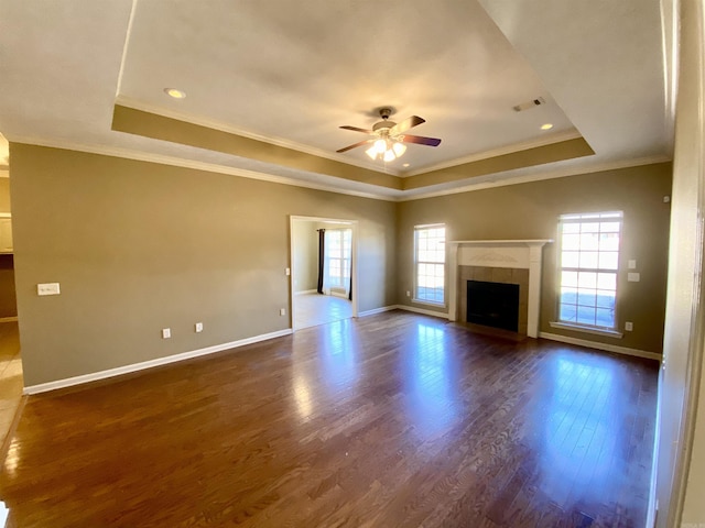 unfurnished living room featuring a tray ceiling, a tiled fireplace, crown molding, and ceiling fan