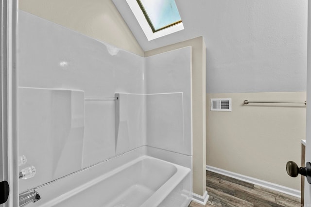 bathroom with hardwood / wood-style floors, lofted ceiling with skylight, and bathtub / shower combination