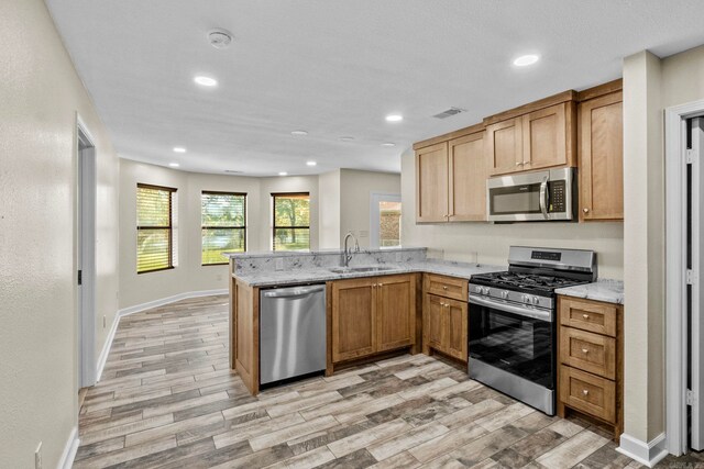 kitchen with light wood-type flooring, kitchen peninsula, sink, and appliances with stainless steel finishes