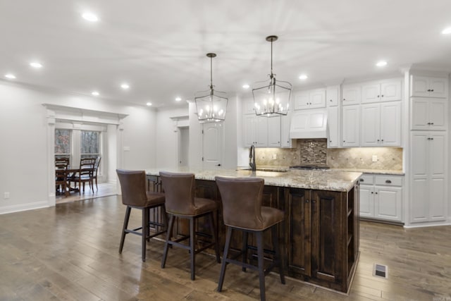 kitchen featuring white cabinets, pendant lighting, a spacious island, and light stone counters