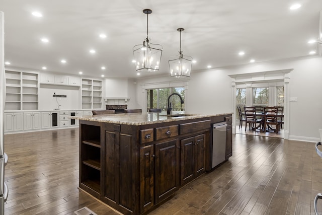 kitchen with dark brown cabinets, sink, a center island with sink, a fireplace, and hanging light fixtures