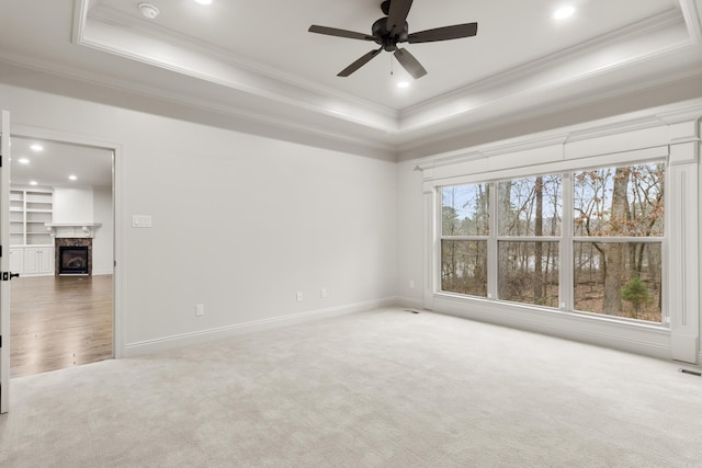 carpeted empty room with a high end fireplace, a tray ceiling, ceiling fan, and crown molding