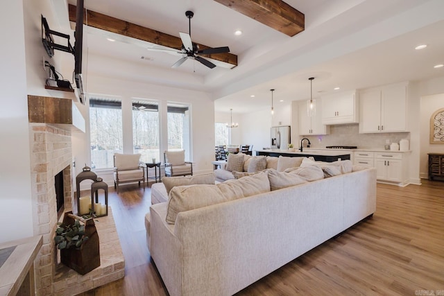 living room featuring ceiling fan, sink, a brick fireplace, beamed ceiling, and wood-type flooring