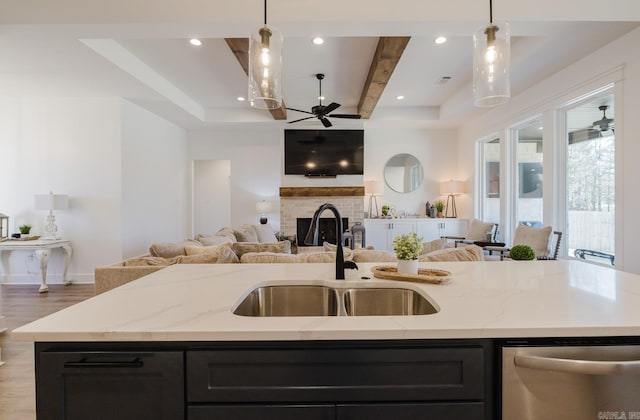 kitchen with dishwasher, sink, light stone counters, decorative light fixtures, and a center island with sink