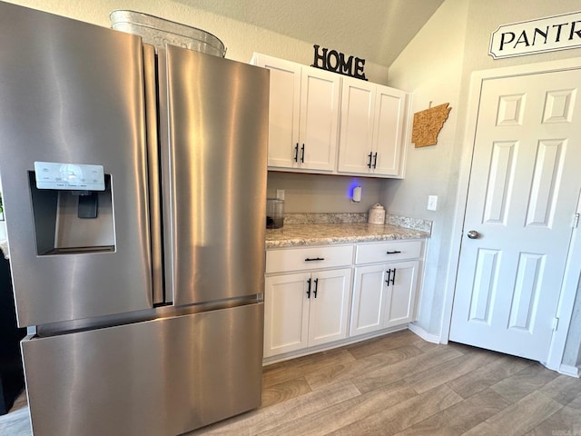 kitchen with white cabinets, light wood-type flooring, stainless steel fridge with ice dispenser, and light stone counters