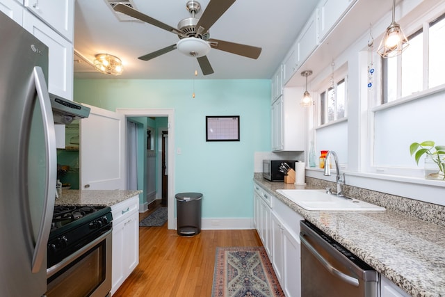 kitchen featuring white cabinetry, appliances with stainless steel finishes, pendant lighting, light stone counters, and sink