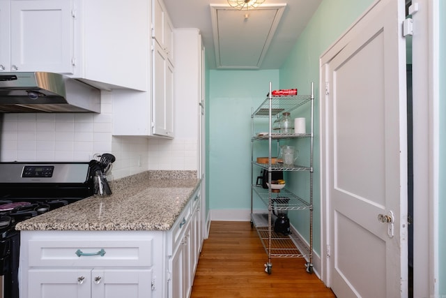 kitchen featuring white cabinets, light hardwood / wood-style floors, decorative backsplash, black gas range, and light stone counters