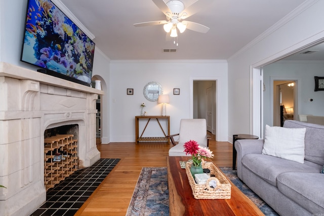 living room featuring ceiling fan, ornamental molding, hardwood / wood-style flooring, and a tile fireplace