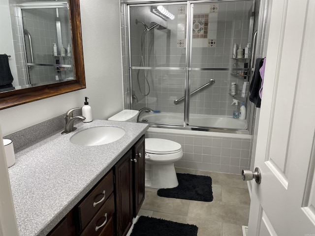 full bathroom with tile patterned flooring, bath / shower combo with glass door, vanity, and toilet