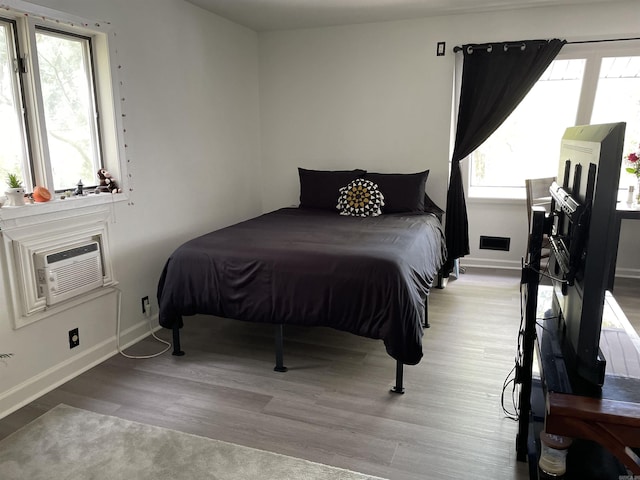 bedroom with multiple windows, a wall mounted air conditioner, and light wood-type flooring