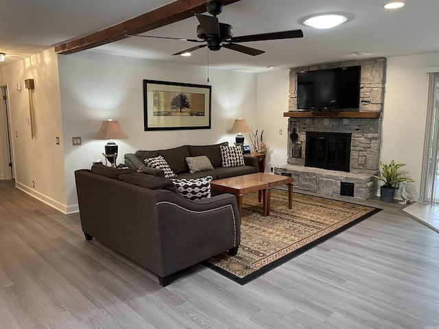 living room with a fireplace, beamed ceiling, ceiling fan, and light wood-type flooring