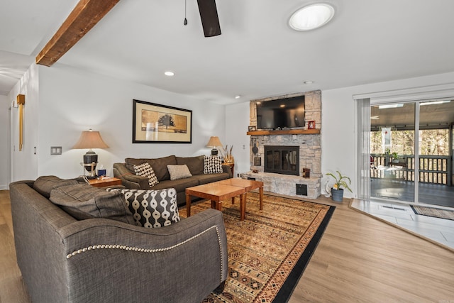 living room with beamed ceiling, ceiling fan, wood-type flooring, and a stone fireplace