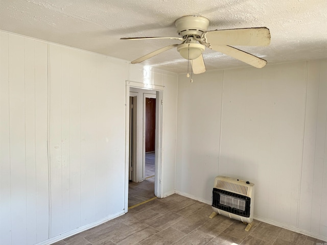 empty room featuring ceiling fan, wood walls, a textured ceiling, and heating unit