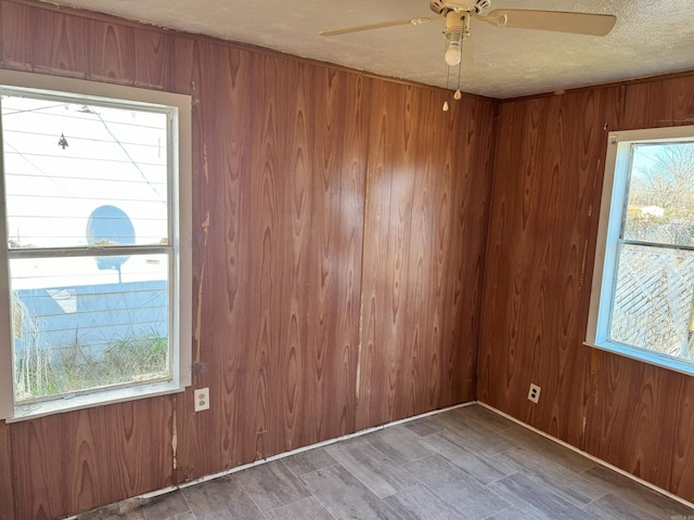 unfurnished room featuring ceiling fan, wood walls, and a textured ceiling