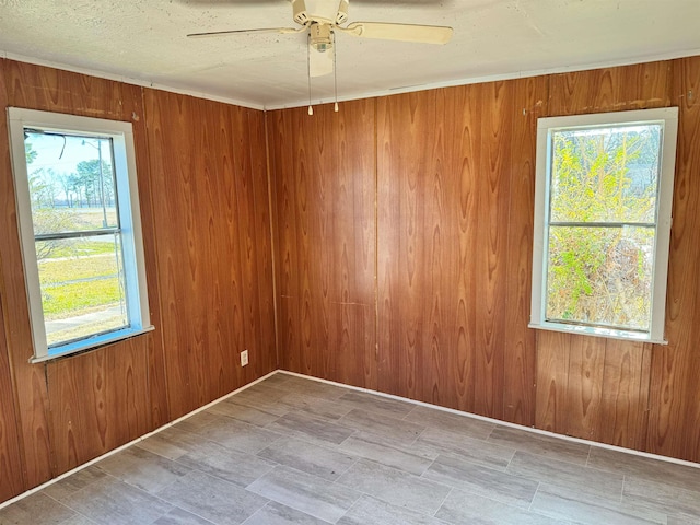 empty room with wooden walls, ceiling fan, and a textured ceiling