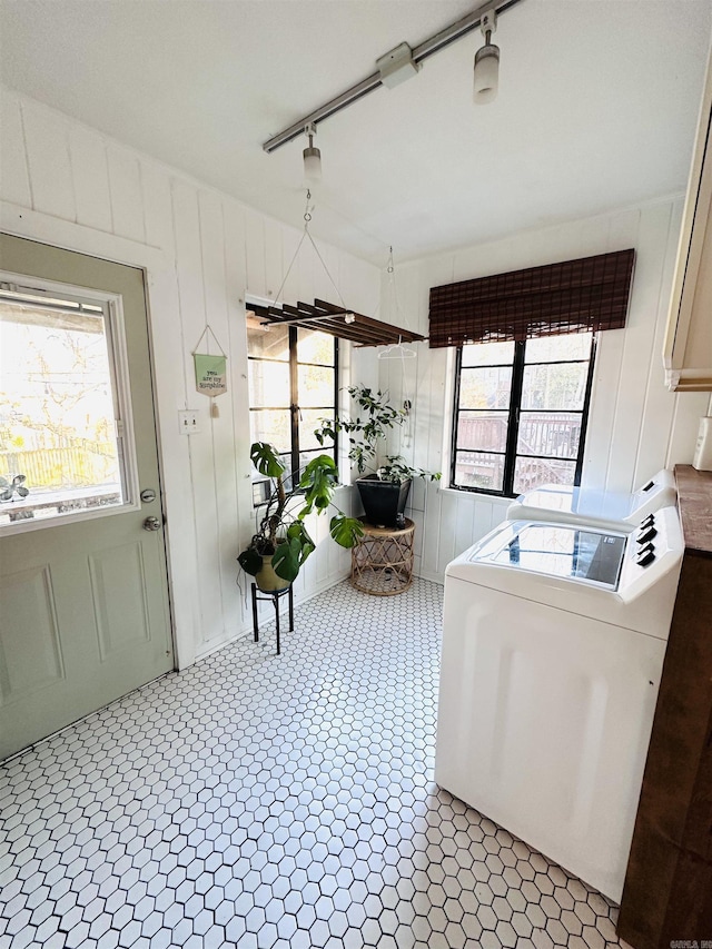 laundry room with light tile patterned flooring, a healthy amount of sunlight, wooden walls, and washer / dryer