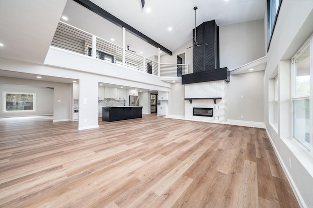 unfurnished living room featuring high vaulted ceiling, a brick fireplace, and light hardwood / wood-style flooring