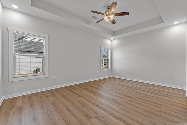 empty room with a tray ceiling, ceiling fan, and light hardwood / wood-style flooring