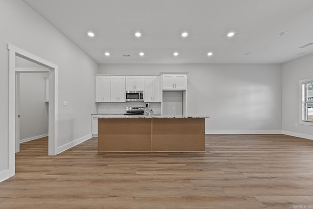 kitchen with a kitchen island with sink, white cabinetry, light stone countertops, and stainless steel appliances