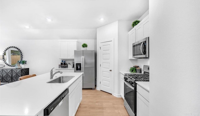 kitchen with light wood-type flooring, stainless steel appliances, sink, white cabinetry, and an island with sink